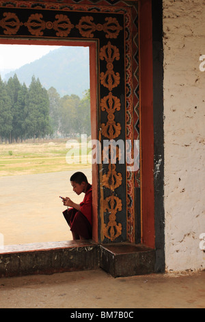 Junge buddhistische Mönch, sitzt in einer offenen Tür, mit seinem Handy. Punakha Dzong, Bhutan Stockfoto