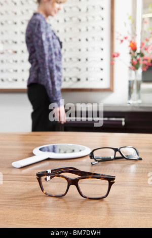 Zwei Paare von Gläsern (eins im Fokus) in einem Brillen speichern, Frau im Hintergrund Stockfoto