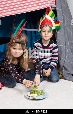 Zwei Kinder sitzen in einer hausgemachten Festung Kopfschmuck tragen Stockfoto