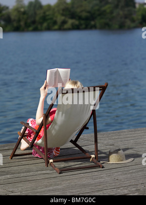 Eine Frau liest im Liegestuhl Strand auf einem dock Stockfoto