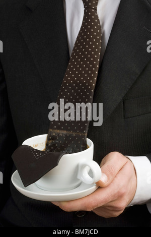 Mann hält eine Tasse Kaffee mit Krawatte im Wasser Stockfoto