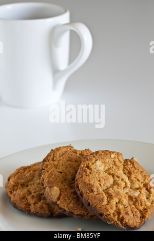 Weiße Tasse und drei mürbe Schokoladenplätzchen auf einem weißen Teller Stockfoto