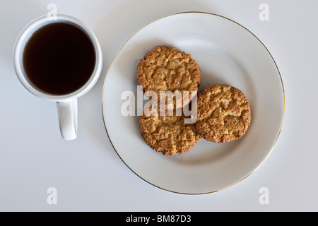 Weiße Tasse schwarzen Kaffee und drei mürbe Schokoladenplätzchen auf einem weißen Teller Stockfoto