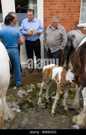Das Fohlen saugt seine Mutter. Pferdehändler trinken einen Drink und plaudern mit Freunden auf der jährlichen Gypsy Charter Horse Fair. Stute und Fohlen zum Verkauf. Einwegbecher und -Flaschen aus Kunststoff verstreuen den Boden. Wickham Hampshire UK. 2010er Jahre HOMER SYKES Stockfoto