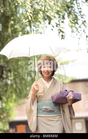 Reife Frau im Kimono holding Regenschirm und Geschenk, Stadt Kyoto, Kyoto Prefecture, Japan Stockfoto