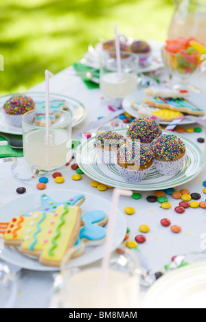 Geeiste Cookies und Muffins auf Tisch geschmückt mit Luftschlangen und Süßigkeiten Stockfoto