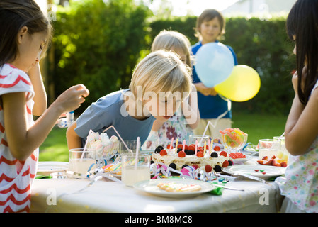 Boy bläst Kerzen auf Geburtstagskuchen auf Outdoor-Geburtstagsparty Stockfoto