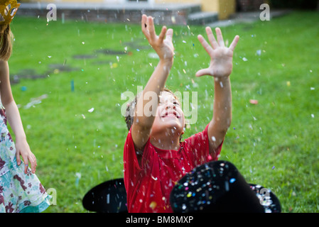 Junge mit erhobenen Armen in fallenden Konfetti überschüttet Stockfoto