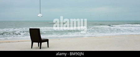 Lampe hängt über dem Stuhl am Strand, Windturbinen entlang Horizont sichtbar Stockfoto