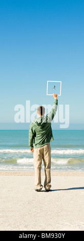 Mann am Strand hält Bilderrahmen Aufnahme Möwe fliegen gegen blauen Himmel Stockfoto