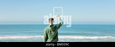 Mann am Strand hält Bilderrahmen Aufnahme Möwe fliegen gegen blauen Himmel Stockfoto