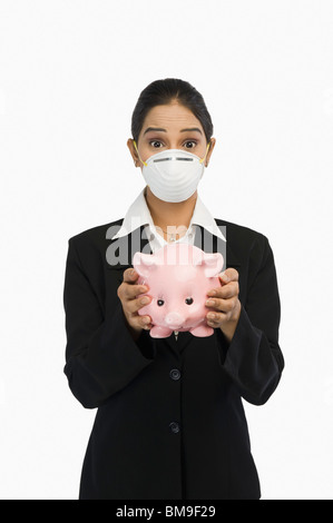 Geschäftsfrau trägt eine H1N1-Maske und hält ein Sparschwein Stockfoto