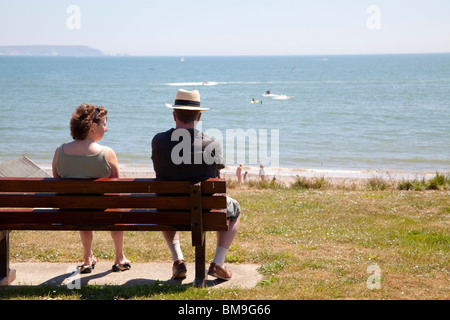 paar, sitzen auf der Bank mit Blick auf Mudeford Strand und die Bucht an einem sonnigen Sommertag Stockfoto