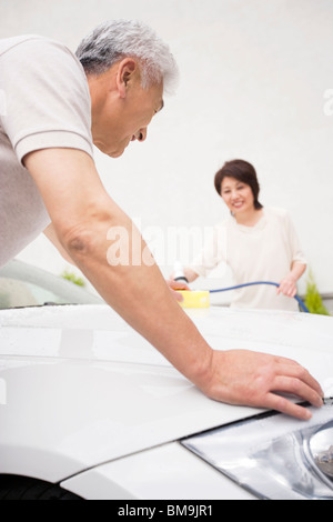 Senior paar Autoreinigung, mit Schlauch und Schwamm Stockfoto