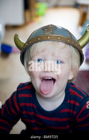 3 Jahre alter Junge mit Spielzeug-Wikinger-Helm seine Zunge herausziehen Stockfoto