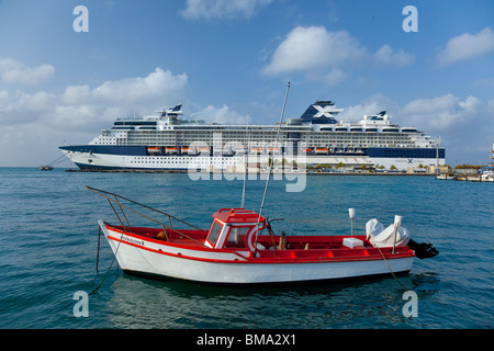 Ein kleines Fischerboot in der Marina und den Hafen von Oranjestad, Aruba mit der Celebrity Cruise Schiff Millennium. Stockfoto