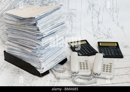Grosser Haufen von Konzeptions- und Zeichnungen, zwei Rechner und zwei Telefone auf der Tischfläche. Weiße Whatman sind Hintergrund. Stockfoto