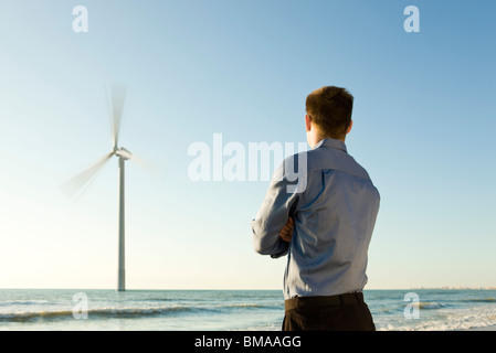 Mann am Strand beobachten Offshore-Windkraftanlage bei der Arbeit Stockfoto