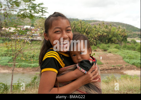 Ein junges laotisches Mädchen, das ihren kleinen Bruder am Fluss in luang prabang Laos hält Stockfoto