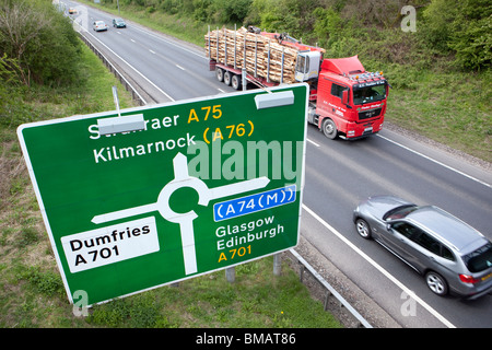 Straßenschild und Wegbeschreibungen am Kreisverkehr auf der A75 in der Nähe von Dumfries mit PKW und LKW vorbei UK zu beschleunigen Stockfoto