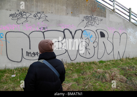 Eine Frau schaut Graffiti auf eine Betonwand in Brentford, Middx, UK gekritzelt. Stockfoto