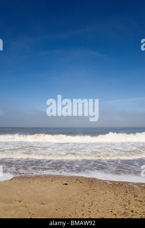 Einen tiefblauen Himmel über einem ruhigen Meer Rollen in einem schönen Sandstrand. Stockfoto