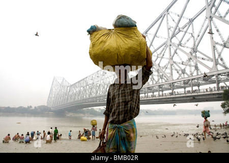 Mann tragenden Last auf Kopf Howrah Brücke über Hooghly Fluß im Hintergrund; Calcutta jetzt Kolkata; Westbengalen; Indien Stockfoto