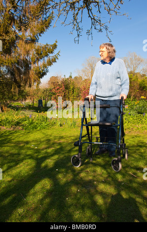 Ein MODEL Release Bild einer älteren Frau mit ihrem Rollator (walking Frame) in einen Bauerngarten in Suffolk, England, Vereinigtes Königreich Stockfoto