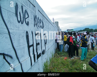 Massen stehen neben einem Schild Pleadng für Hilfe in Port-au-Prince nach dem Erdbeben in Haiti Stockfoto