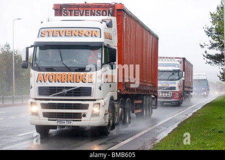 Hauptverkehrszeit Verkehr beschäftigt zweispurigen Straße A75 UK Schlechtwetter regen Nebel Dunkeln sprühen eine Reihe von Lastwagen mit Lichtern auf Stockfoto