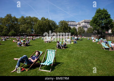 Menschen Sie auf dem Rasen liegen und sitzen auf den Liegestühlen in der Sonne in St James Park, Zentrum von London. Stockfoto