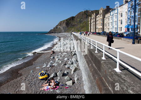 Menschen am Strand Sonnenbaden und Wandern am Meer Promenade Aberystwyth Wales UK Stockfoto