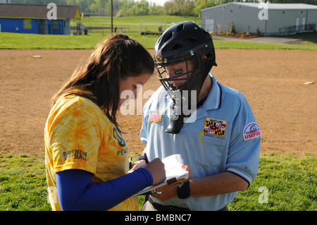 Trainer beschreibt eine Änderung in den Dienstplan mit Home-Plate Umpire in einem Softballspiel Stockfoto