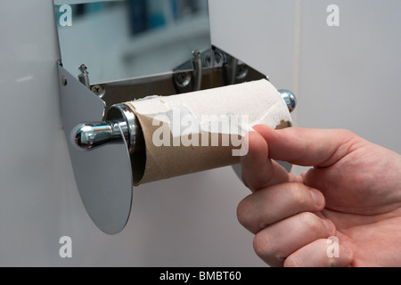Die Hand von Mans zieht das letzte noch vorhandene Blatt toilettenpapier auf einem toilettenrollenhalter aus der Rollenkrise des Klo Stockfoto