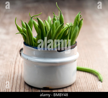 Frisch gepflückten grünen Bohnen In eine alte Emaille-Tasse auf eine Holzoberfläche Stockfoto