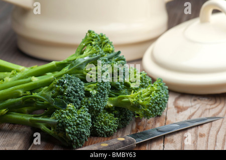 Frischer Tenderstem Brokkoli mit einem Gemüsemesser und eine Pfanne mit Deckel im Hintergrund auf Holz Küchentisch gelegt. Stockfoto
