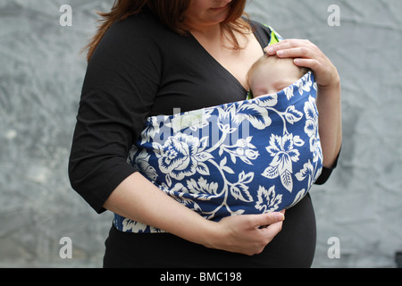 Eine Mutter hält ihr neugeborenes Baby in einer kleinen Schlinge. Stockfoto