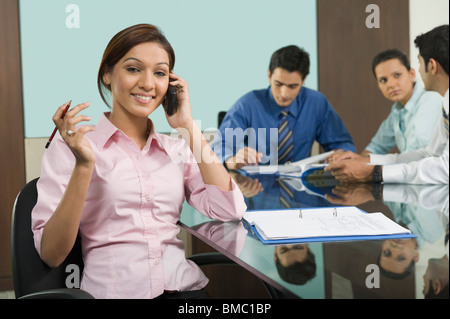 Porträt von eine Geschäftsfrau, die auf einem Mobiltelefon im Gespräch mit ihren Kollegen arbeiten hinter ihr Stockfoto