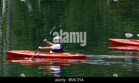 Ein Mann Mann in einem orangefarbenen Kajak. Paddeln entlang der Küste bei Merrill Creek Reservoir, New Jersey. Stockfoto