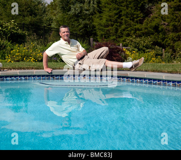 Mann mittleren Alter entspannt an der Seite eines Pools in einen blühenden Garten Stockfoto