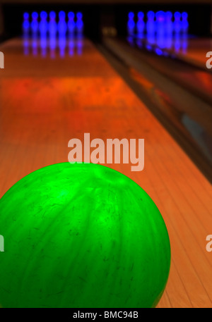 Grüne Bowling-Kugel mit Pins im Hintergrund Stockfoto