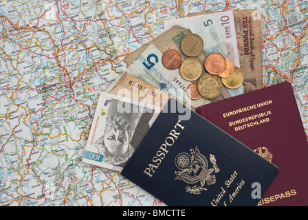 Reisepässe (Deutschland und USA) mit Geld in verschiedenen Währungen auf einer Karte. Stockfoto