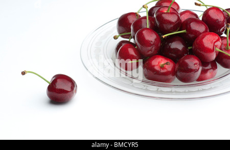 Frische Kirschen auf einer Glasplatte mit einer einzigen Kirsche auf die Seite, auf einem weißen Hintergrund Stockfoto