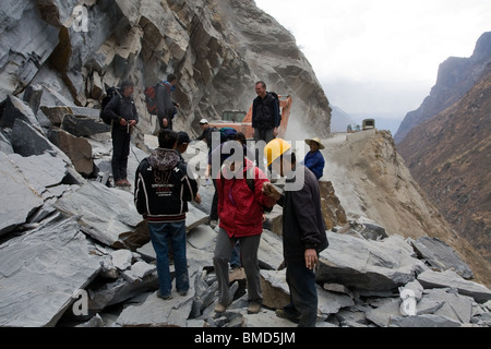 Chinesische Arbeiter helfen Touristen Wanderer einen Haufen von Felsen in einer Yangzi Damm Baustelle in der Nähe von Trek Tigersprung-Schlucht zu überqueren. Stockfoto