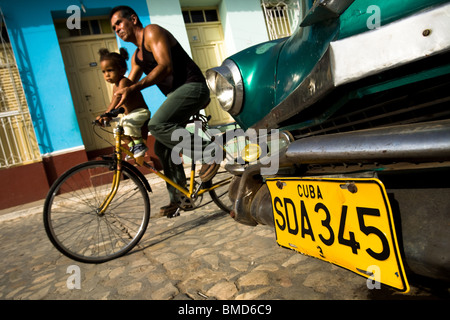 Ein Mann und ein junges Mädchen Fahrrad vorbei ein 1950er Jahre Auto parkte auf der Straße von Trinidad, Kuba auf Mittwoch, 2. Juli 2008. Stockfoto