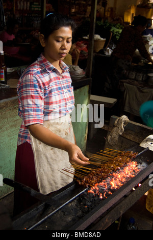Tief in den Schalen von der Ubud kocht Bali öffentlicher Markt eine Frau Huhn Sate über eine Kokosnuss angeheizt Feuer, hungrige Shopper zu ernähren. Stockfoto