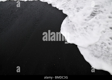 Eine Welle fließt über tiefen schwarzen vulkanischen Sand am Strand Stockfoto