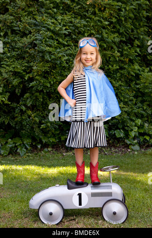 Mädchen mit blauen Umhang stehend auf Spielzeugauto Stockfoto