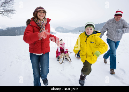 Eltern und Bruder ziehen Mädchen im Schlitten im Winter Stockfoto