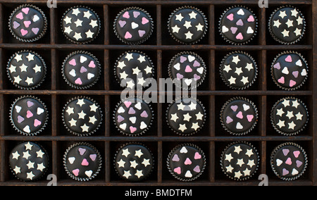 Mini-Muffins mit schwarzer Glasur, Zuckerherzen und weiße Schokolade Sterne in einem Holztablett dekoriert Stockfoto
